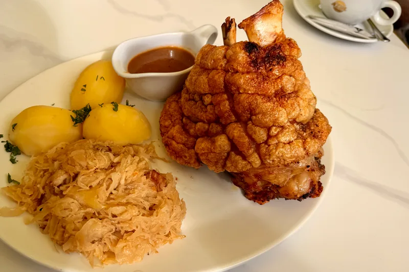 Servierte Schweinshaxe mit krosser Kruste, Salzkartoffeln, Sauerkraut und Sauce in der Adlermühle